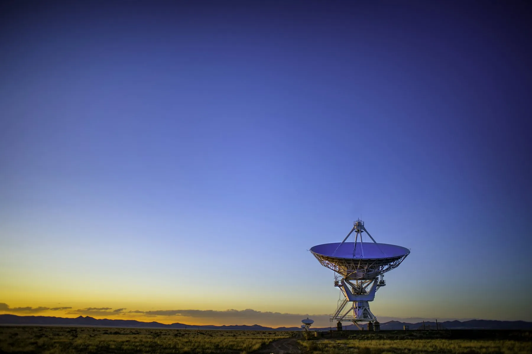 A satellite dish on open ground at dusk